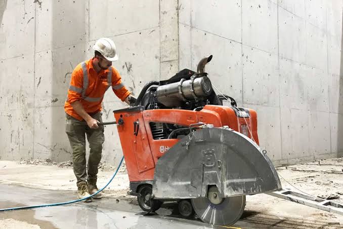 Worker operating large diamond saw for concrete cutting on roadway